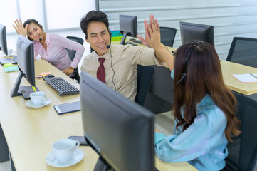 Obraz premium Customer support representative talking on headset while using computer. Businessman working at desk with colleague in background. He is wearing casuals in call center.