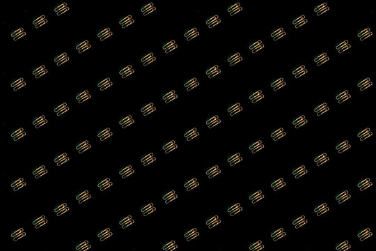 A pattern of gold colored paper clips are on a black paper background. Paperclip.