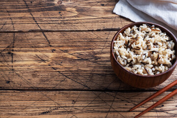 Obraz na płótnie Canvas Brown and unpeeled rice on a plate with chopsticks. Wooden rustic background. Copy space.