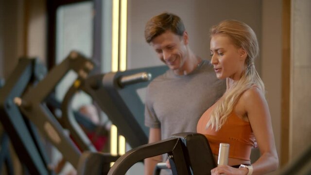Hot fit girl making bicep curls in sport club. Fit man helping his client at gym