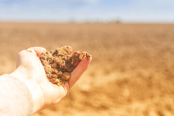 Plowed land close-up. Brown soil in the hand of a man. Poor, barren soil.