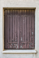 View of closed window with cracked peeling paint wooden shutters cracked on wall of the old shabby house