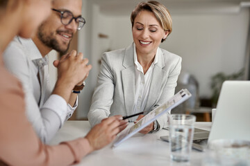 Happy real estate agent and a couple going through blueprints on a meeting.