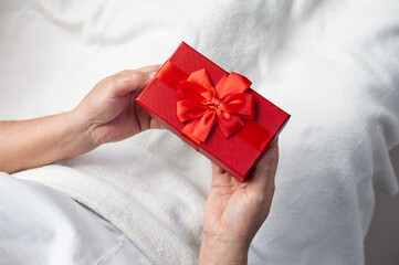 Closeup on hands elderly or old woman holding anniversary red gift box of Birthday, Christmas and New year aniversary sitting on white bed