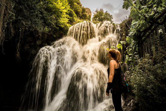 Chica observando una cascada desde su base en un dia soleado