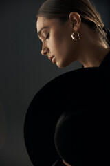 profile of a beautiful girl with closed eyes, she has a professional makeup, earrings in her ear, she and covered with a black hat on a dark background in the studio