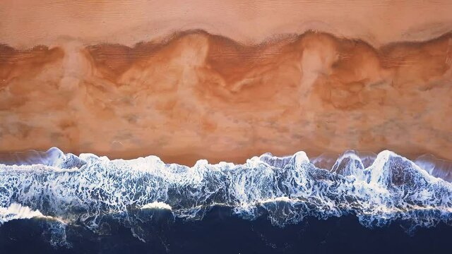 Flying over a sandy beach. Waves break on a sandy beach on the Atlantic coast, aerial View. Nazare, Portugal.