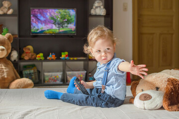 Cute baby boy and his dog plush toy watching TV sitting on a couch in the living room at home