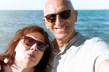 Middle-aged couple takes a selfie on the beach during a vacation - Happy elderly couple having fun in their free time - Active retirees having fun traveling the world concept - flare on background.