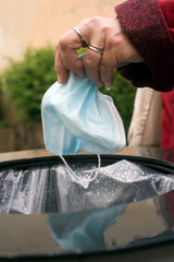 Closeup of hand of woman putting used medical mask in the garbage in the street during the covid-19 pandemic