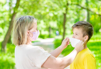 Obraz premium Mother wearing protective face mask helps put on a mask for her young son while they are in a public place
