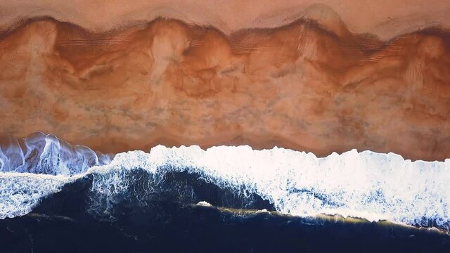 Flying over a sandy beach. Waves break on a sandy beach on the Atlantic coast, aerial View. Nazare, Portugal.