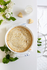Homemade cheesecake in a white dish on a table with lilacs, top view, flat lay