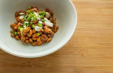 Close up organic Nutto or Fermented Soy in white bowl on wooden table, Japanese traditional healthy food. Nutto topping with green onion.