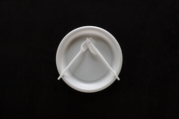 Disposable white plastic plate, fork and knife on a black velvet. View from above. Rules of etiquette.