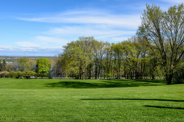 Rolling grassy hill and trees in Battlefields Park with a view overlooking Quebec, Canada and blue sky with clouds in background..