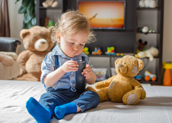 Cute baby boy playing with the remote control on a couch in the living room at home