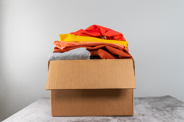 Colored bright clothes in a donation box on a gray table