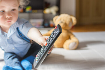 Cute baby boy playing with the remote control on a couch in the living room at home