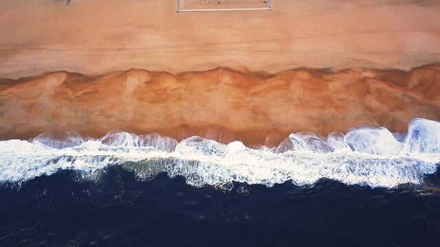 Flying over a sandy beach. Waves break on a sandy beach on the Atlantic coast, aerial View. Nazare, Portugal.
