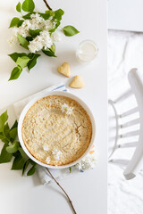 Plate with whole cheesecake pie on table with lilacs. Classic cheesecake, flat lay or top view.
