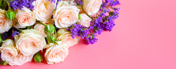 a bouquet of cream roses and bright purple flowers in full bloom on a pink background with space for text. greeting card. banner