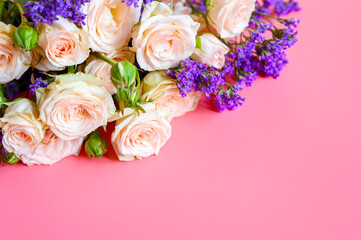 a bouquet of cream roses and bright purple flowers in full bloom on a pink background with space for text. greeting card