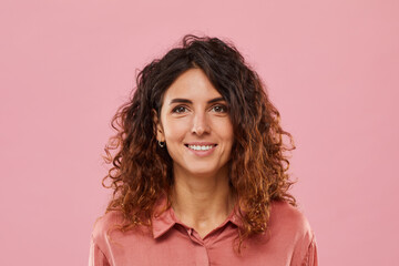Portrait of young woman with curly hair smiling at camera isolated on pink background