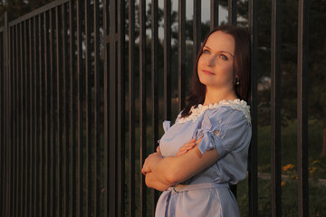 A woman looks at the sunset with her back to the fence.