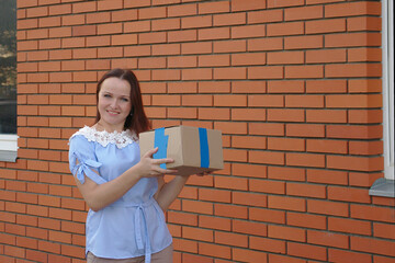 A woman with a cardboard box is standing against a brick wall. Parcel delivery.