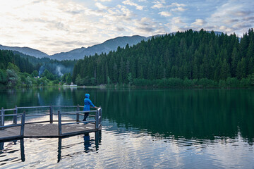 Woman in blue coat stands and poses on the dock. Landscape photo was taken at Karagol / Karagöl...