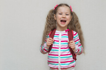 Back to school. Portrait fair-haired school girl with bag. Light grey studio background. Education. looking and laughs at camera. copy place.