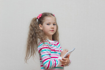 A portrait of a fair-haired schoolgirl stands with a notebook in her hands and writes in it. Light grey Studio background. Education. looking camera. copy place