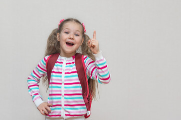 Back to school. Portrait of a blonde schoolgirl in a jacket. The girl is smiling and looking at the camera. Thumbs up. Light background. Education. copy place.