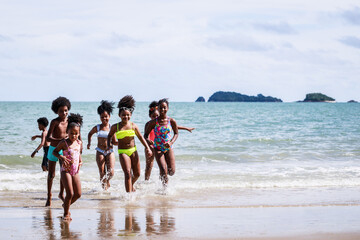 African American, Kids group in swimwear enjoying running to play the waves on beach. Ethnically diverse concept. Having fun after unlocking down from COVID 19. Summer holidays on beach with friends