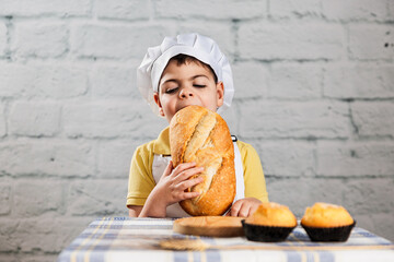 un niño vestido con gorro y delantal de panadero tiene toda una barra de pan en la boca mientras...