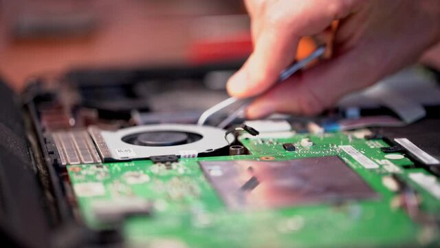 A computer science technician who takes out an old cooler dirty in dust to cool the processor in a laptop computer. Close-up.