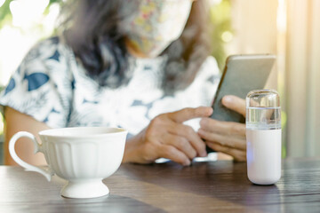 A quarantined woman relax with hot cappuccino coffee and alcohol nano mist sprayer on table while...