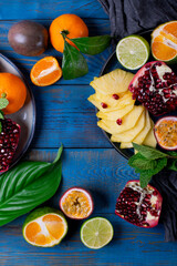 Pineapple slices, pomegranate, passion fruit and tangerines forming copy space on the blue wooden background