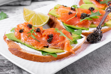Sandwich with salted trout, avocado, cream cheese, black caviar and arugula on the white platter