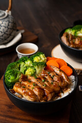 Japanese Food Style : Top view of Homemade Chicken Teriyaki grilled with rice , carrot , broccoli put on the black bowl and place on wooden table