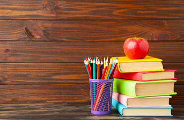 Multi coloured school books and stationery on brown wooden background