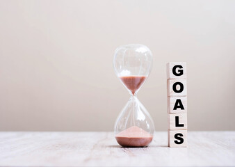 Hourglass with GOALS wooden cube blocks on table, Sand flowing through the bulb of Sandglass measuring the passing time. countdown, deadline, Life time and Retirement concept