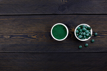Pills and powder of green chlorella or spirulina  on wooden background. Nutritional supplement, alternative medicine and healthy lifestyle.