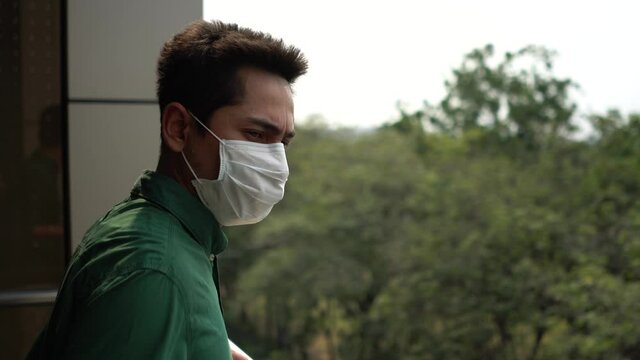 A man wearing mask protective for spreading of disease virus Covid-19 and air smog pollution with PM 2.5 standing  looking nature on skywalk at chatuchak district in  Bangkok city, Thailand.