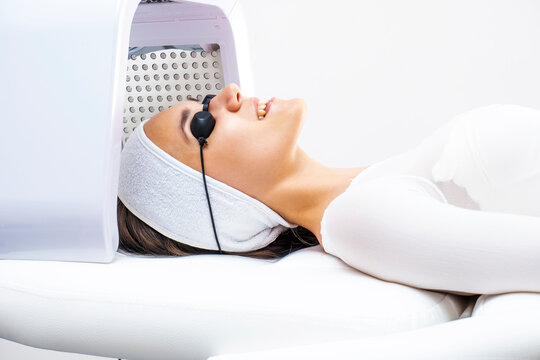 Led phototherapy for the face. Phototherapy in cosmetology. A beautiful young woman in a suit and glasses lies in the cosmetologist’s office on the face phototherapy procedure.