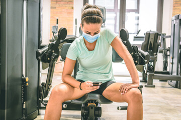 Young brunette woman looks at her cell phone in the gym. She's sitting in a strength machine.