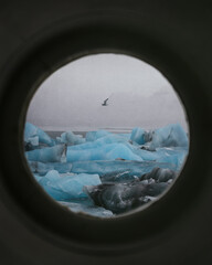 View of blue icebergs through a round window, porthole in Iceland. Blue ice in glacier lagoon Jokulsarlon. Vertical nature photo