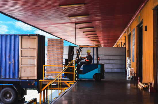 Forklift stuffing-unstuffing pallets of cargo to container on warehouse leveler dock.