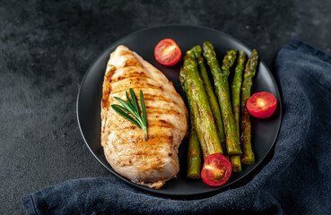 Grilled chicken breast with asparagus and spices on a black plate on a stone background with copy space for your text